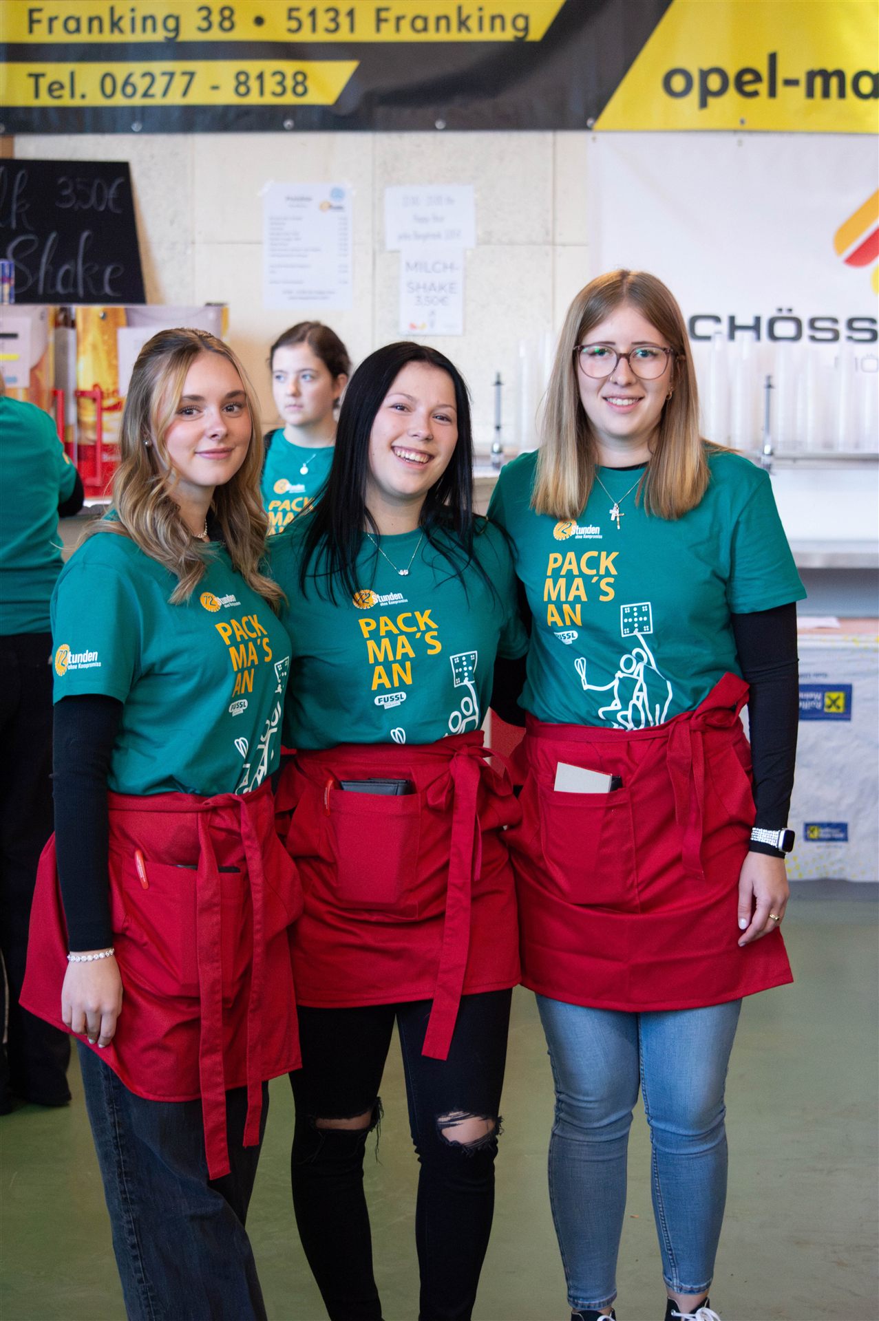 Drei Helferinnen in Pack-ma's-an-Shirts und roten Schürzen