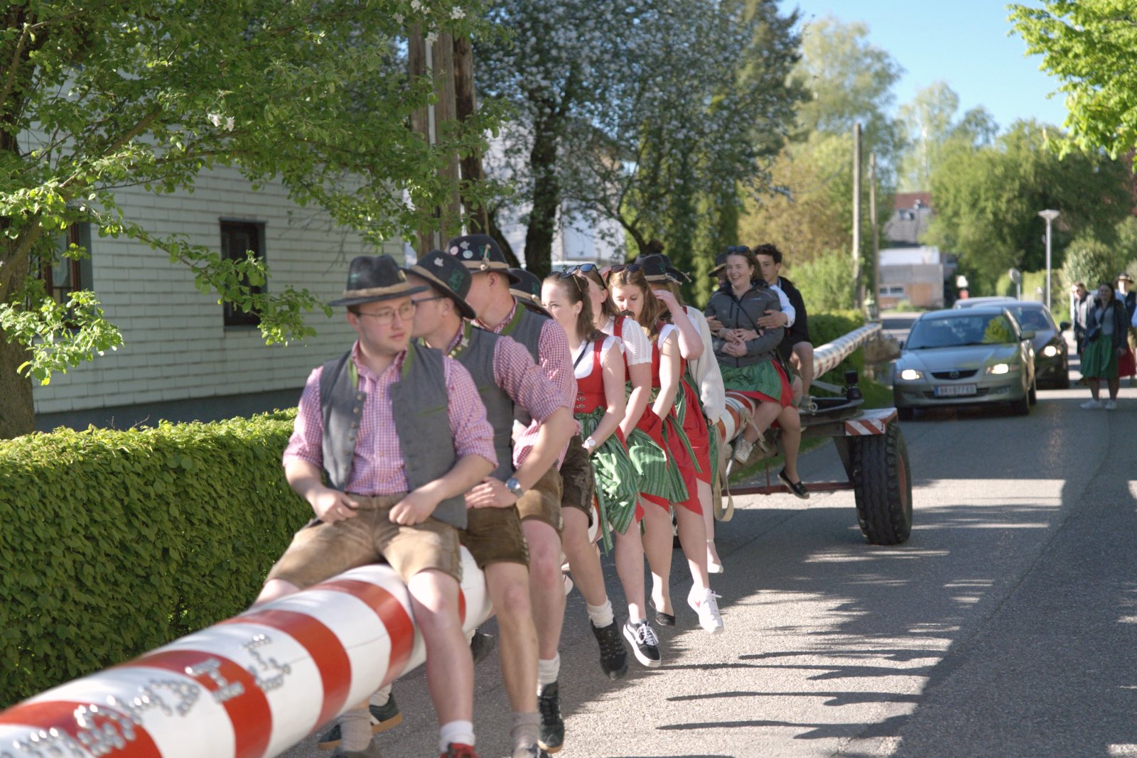 Landjugend-Mitglieder in Tracht sitzen auf dem rot-weißen Maibaum beim Transport durchs Dorf